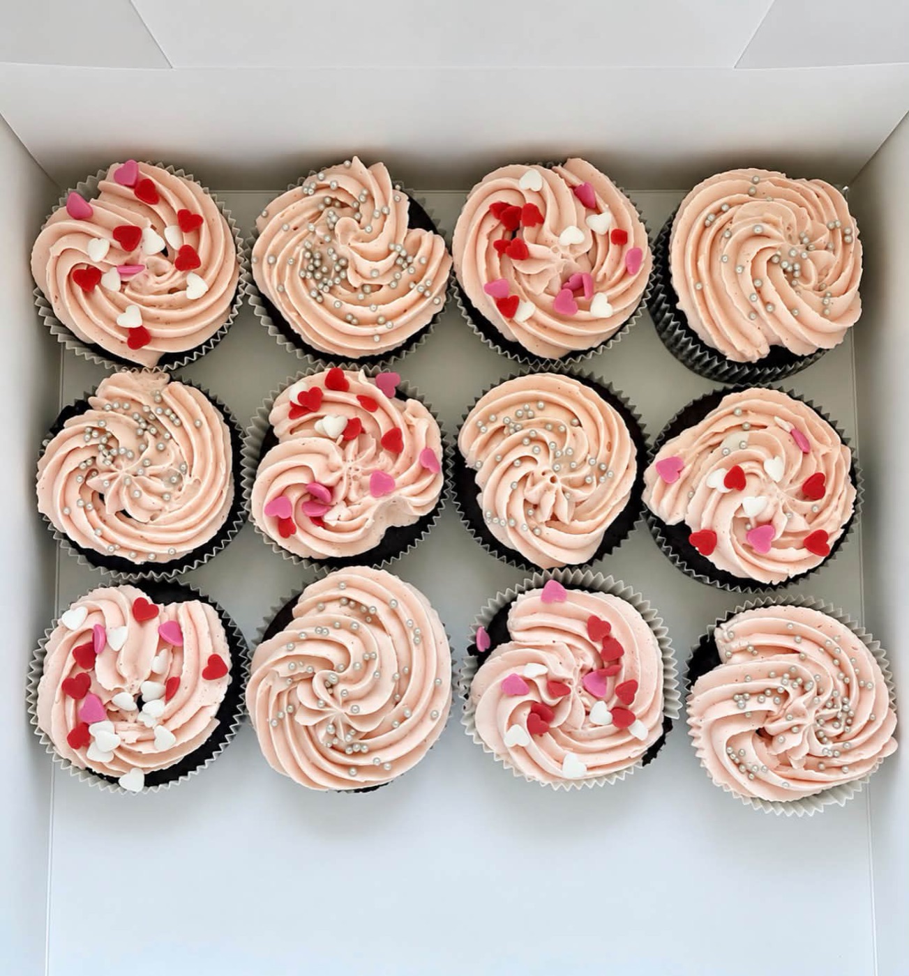 Zwölf Cupcakes mit rosa Creme in einer Schachtel
