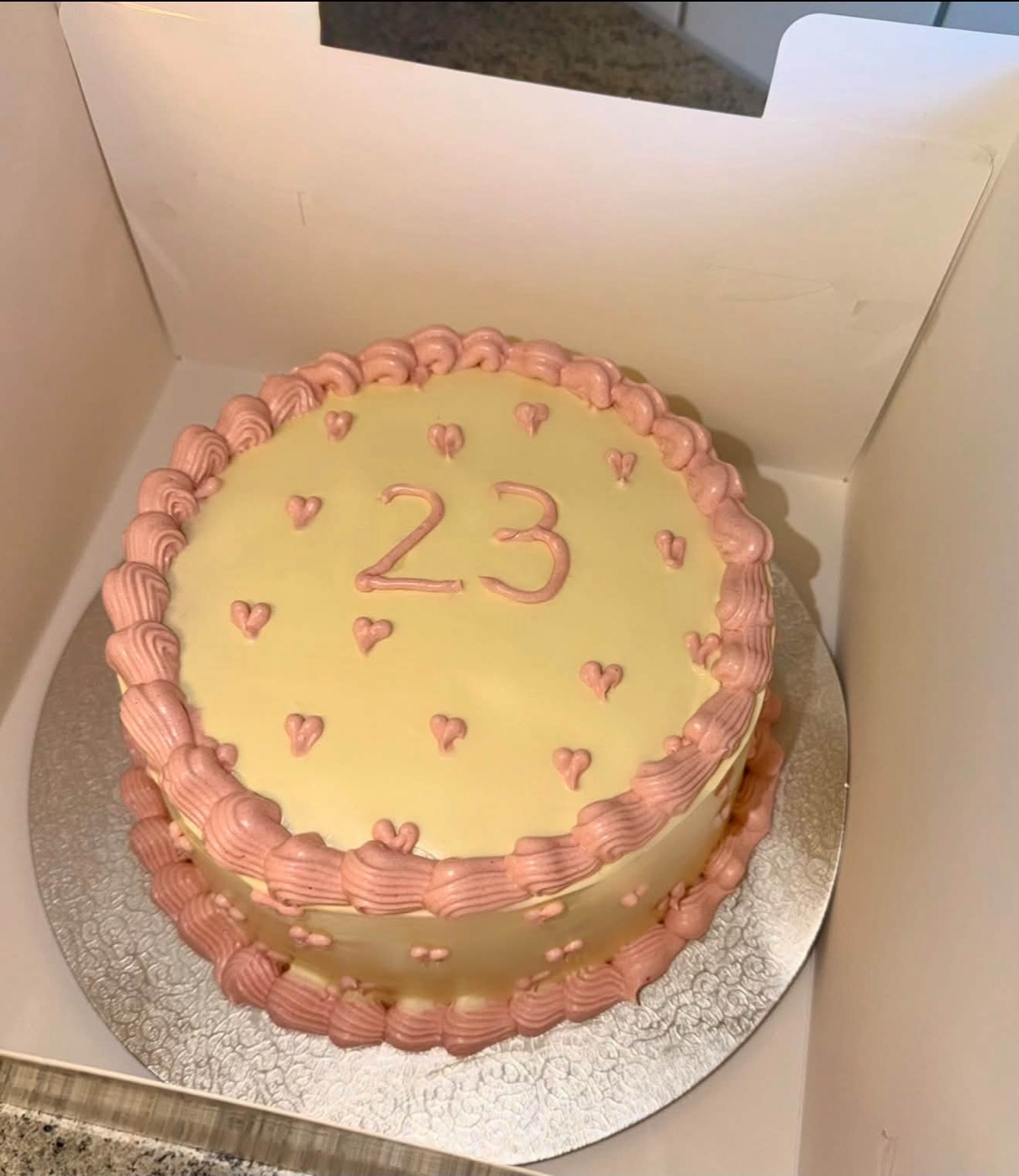 Gelbe Torte mit rosa Rand, kleinen Herzen und der Zahl 23