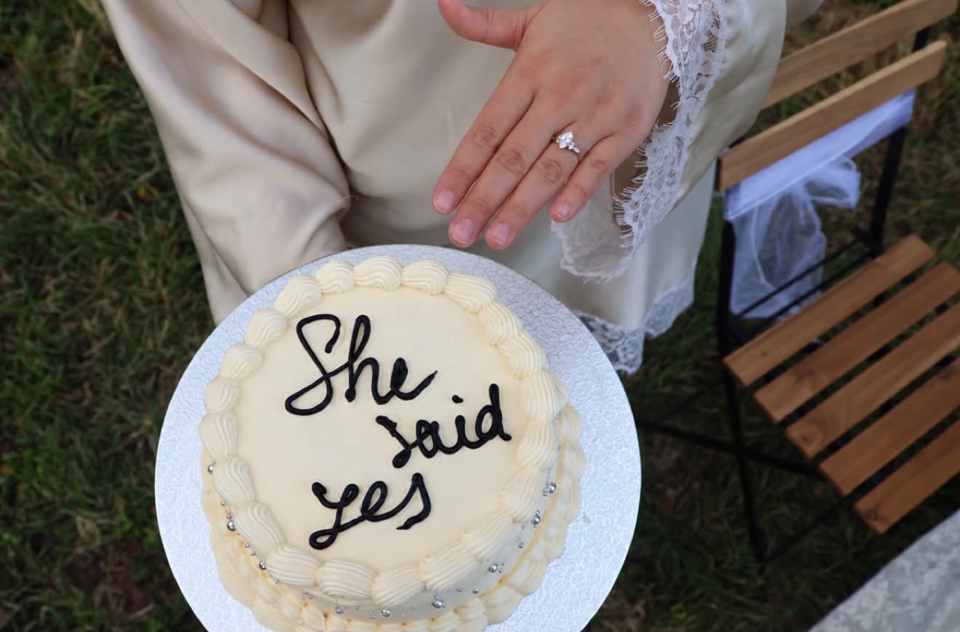 Weisse Torte mit der Aufschrift She said yes, daneben eine Hand mit Verlobungsring